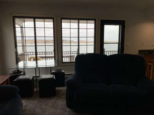 Cozy living room with a view of a lake through large windows, featuring a couch and small tables.