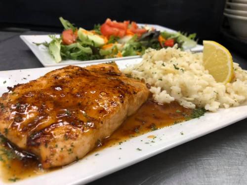 Grilled salmon fillet with a glaze, served with rice and a side salad of mixed greens and tomatoes.