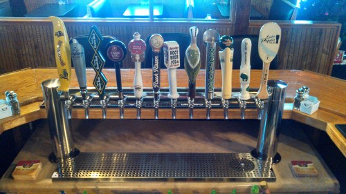 A row of beer taps with various handles on a wooden bar, showcasing different brands and styles of beer.