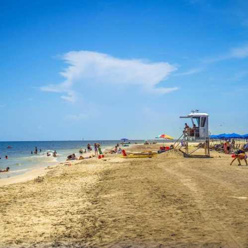 A sunny beach scene with people enjoying the water, colorful umbrellas, and a lifeguard tower in the background.