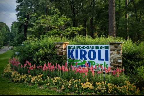 A colorful sign reading "Welcome to Kiroli Park" surrounded by vibrant flowers and lush greenery.