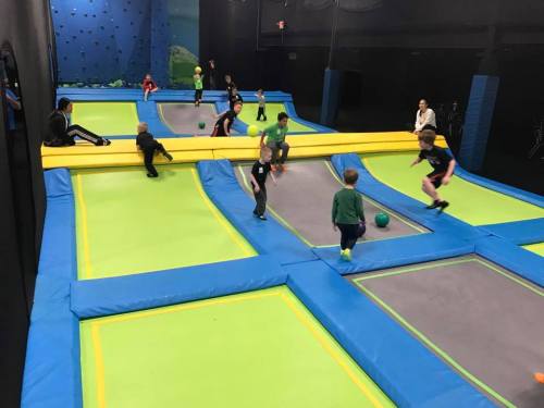 A vibrant indoor trampoline park with children playing and bouncing on trampolines and dodgeball areas.