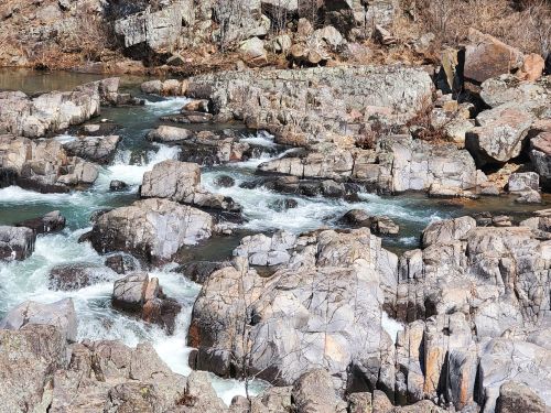 A rocky riverbed with flowing water, surrounded by boulders and sparse vegetation.