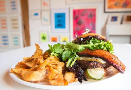 A delicious burger with lettuce, pickles, and bacon, served with crispy potato chips on a white plate.