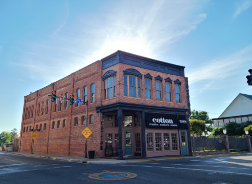 Historic brick building with large windows, featuring a sign for "Cotton" and traffic signals nearby.