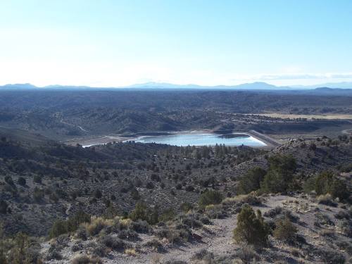 A panoramic view of a vast landscape featuring a lake surrounded by mountains and sparse vegetation under a clear sky.