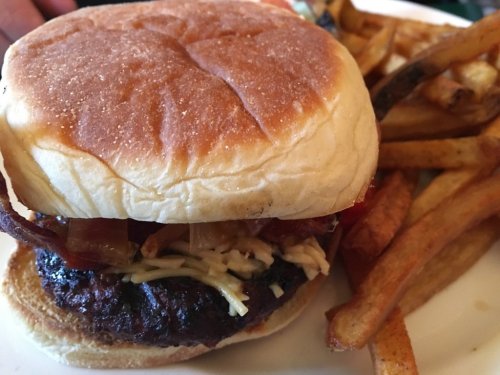 A close-up of a burger with toppings, served with a side of golden fries on a plate.