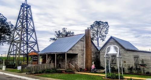 A rustic wooden building with a metal roof, next to a tall, metal structure, set against a cloudy sky.