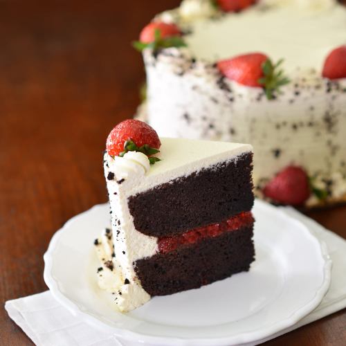 A slice of chocolate cake with strawberry filling, topped with whipped cream and a fresh strawberry, on a white plate.