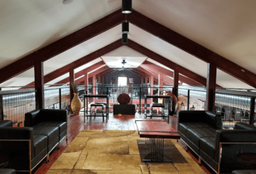 A spacious loft with wooden beams, black sofas, a coffee table, and decorative items, creating a cozy atmosphere.