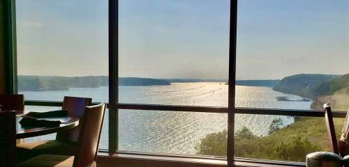 A scenic view of a shimmering river through a large window, with hills in the background under a clear sky.