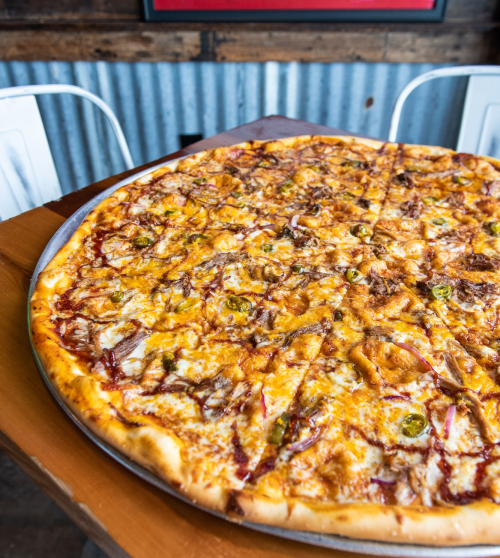 A large pizza topped with cheese, chicken, jalapeños, and barbecue sauce on a wooden table.