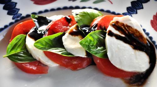 A fresh Caprese salad with slices of tomato, mozzarella, basil leaves, and a drizzle of balsamic glaze on a decorative plate.