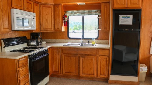 A cozy kitchen with wooden cabinets, a stove, microwave, sink, and a black refrigerator, set in a bright space.