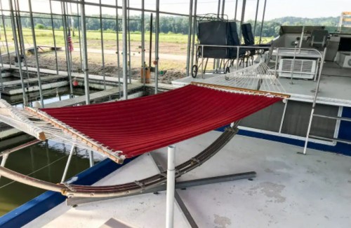 A red hammock is set up on a dock, surrounded by a serene view of water and greenery in the background.