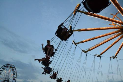 A swing ride at dusk with riders enjoying the view, illuminated by bright lights against a cloudy sky.