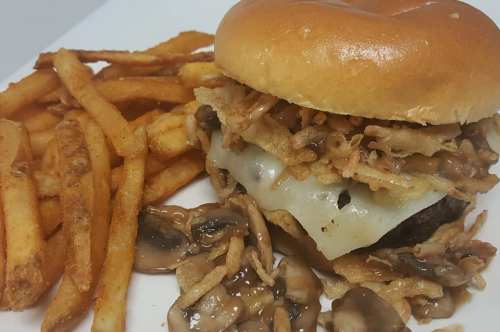 A juicy burger topped with melted cheese, crispy onions, and mushrooms, served with a side of golden French fries.