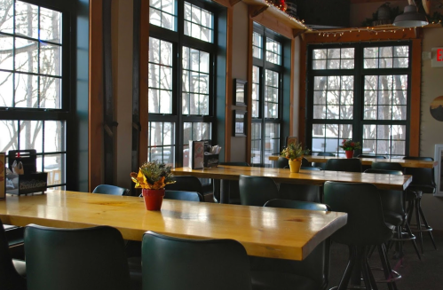 Cozy restaurant interior with wooden tables, green chairs, and large windows letting in natural light.