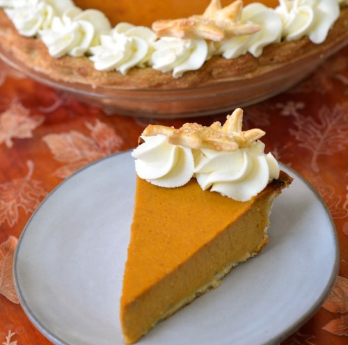 A slice of pumpkin pie topped with whipped cream and decorative pastry stars, served on a white plate.