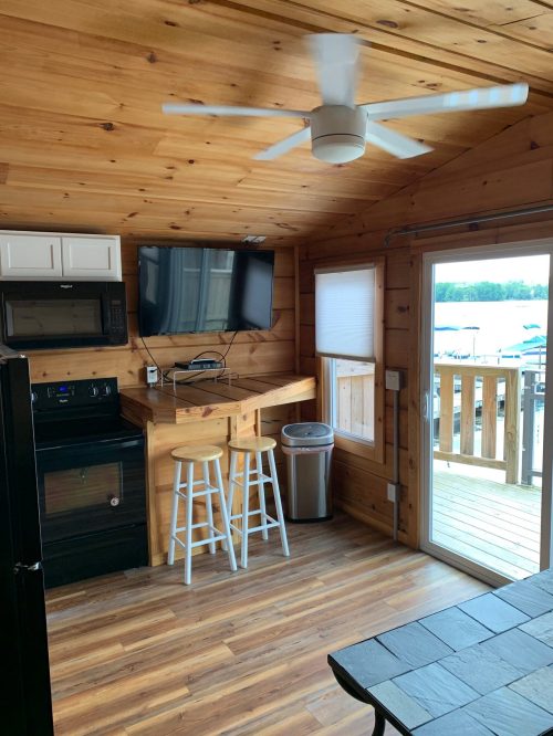 Cozy cabin interior with wooden walls, a kitchen area, a TV, and a sliding door leading to a deck.