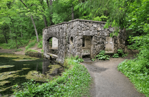 A stone structure by a pond, surrounded by lush greenery and a winding path.