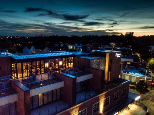 Aerial view of a modern building at sunset, with city lights and a colorful sky in the background.