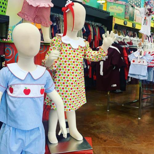 Two mannequins display colorful children's clothing in a vibrant store setting.