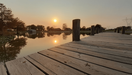 A serene sunset over a calm lake, viewed from a wooden dock with posts lining the edge.
