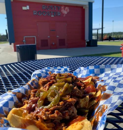 A plate of loaded nachos topped with meat, jalapeños, and sauce, with a restaurant named Rusty Rooster in the background.