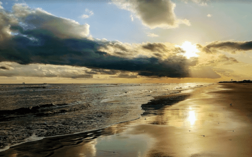 A serene beach at sunset, with golden light reflecting on wet sand and clouds in the sky.