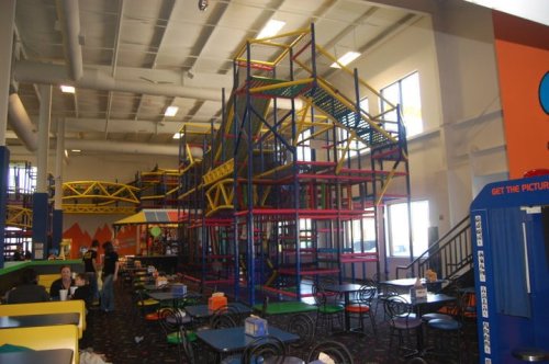 Indoor play area featuring colorful climbing structures, slides, and seating for families. Bright and spacious environment.
