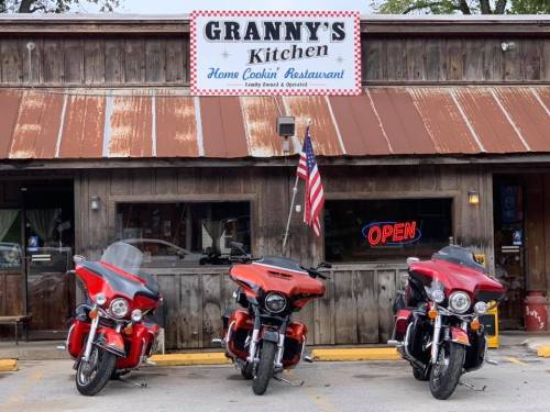 Three red motorcycles parked in front of Granny's Kitchen, a rustic restaurant with a sign that reads "Home Cookin' Restaurant."
