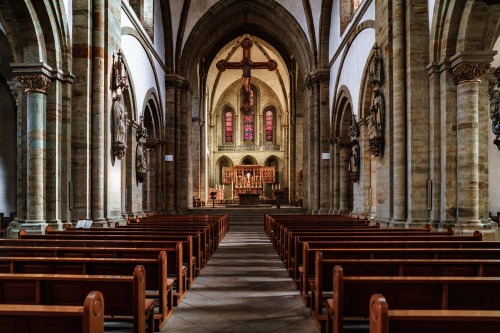 Interior of a historic church featuring wooden pews, stone arches, and a beautifully adorned altar with stained glass windows.