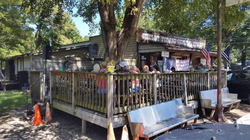 A rustic outdoor dining area with people gathered on a deck, surrounded by trees and American flags.