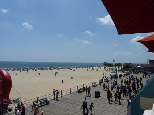 A sunny beach scene with people on the boardwalk, umbrellas, and a sandy shore stretching to the ocean.