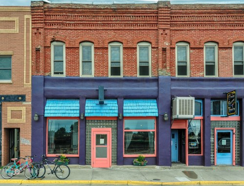 Colorful storefronts with brick and painted facades, featuring blue awnings and bicycles parked outside.