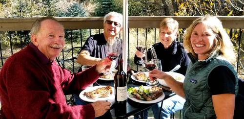 A group of four friends enjoying a meal outdoors, toasting with glasses of red wine at a table.