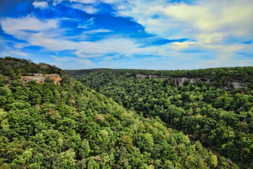 Lush green hills and cliffs under a bright blue sky with scattered clouds. A serene natural landscape.