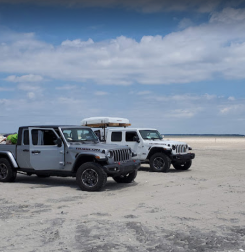Two off-road vehicles parked on a sandy beach under a cloudy sky.