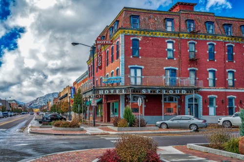 Historic red brick hotel on a street corner, with mountains in the background and a cloudy sky above.