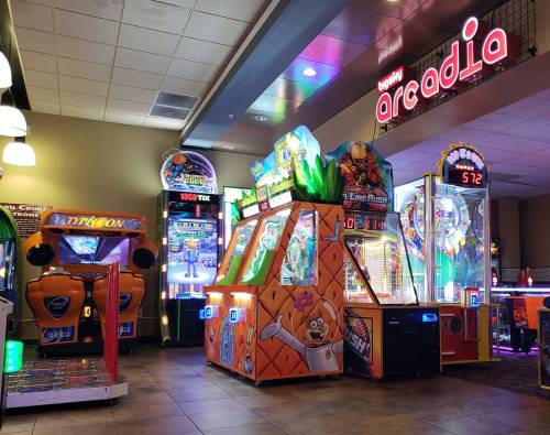 A brightly lit arcade featuring various colorful game machines and a sign reading "Arcadia."