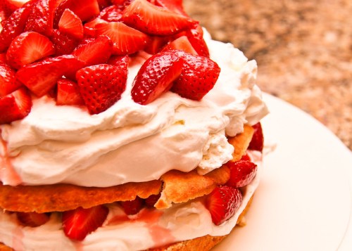 A layered cake topped with whipped cream and fresh strawberries on a white plate.