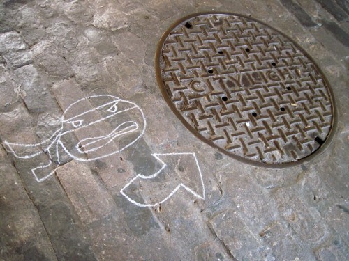 Chalk drawing of an angry ninja next to a round manhole cover labeled "CITY LIGHT."
