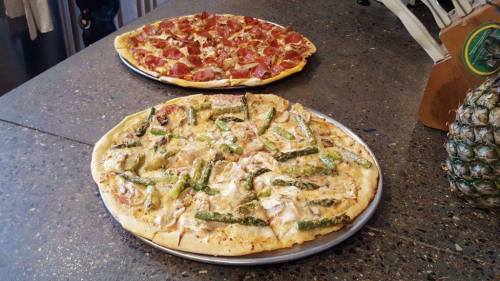 Two pizzas on a table: one topped with pepperoni and cheese, the other with chicken and asparagus.