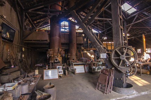 Interior of an old workshop with large machinery, tools, and a rustic atmosphere, showcasing industrial heritage.