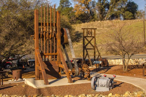 Rusty industrial machinery displayed outdoors, surrounded by trees and gravel, with informational signs nearby.