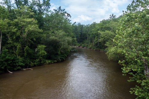 A serene river flows through a lush green forest under a partly cloudy sky.
