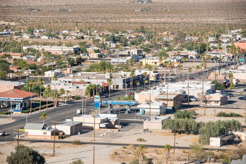 Aerial view of a small desert town with streets, buildings, and palm trees under a clear sky.