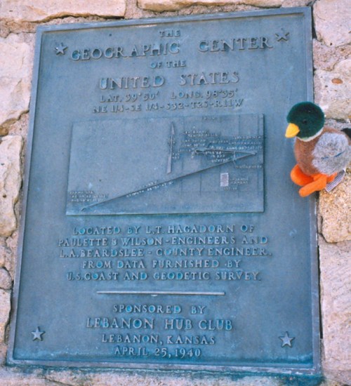 A plaque marking the Geographic Center of the United States, with a small stuffed duck perched on it.