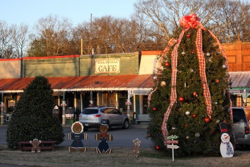 A festive scene featuring a decorated Christmas tree, holiday decorations, and a café in the background.